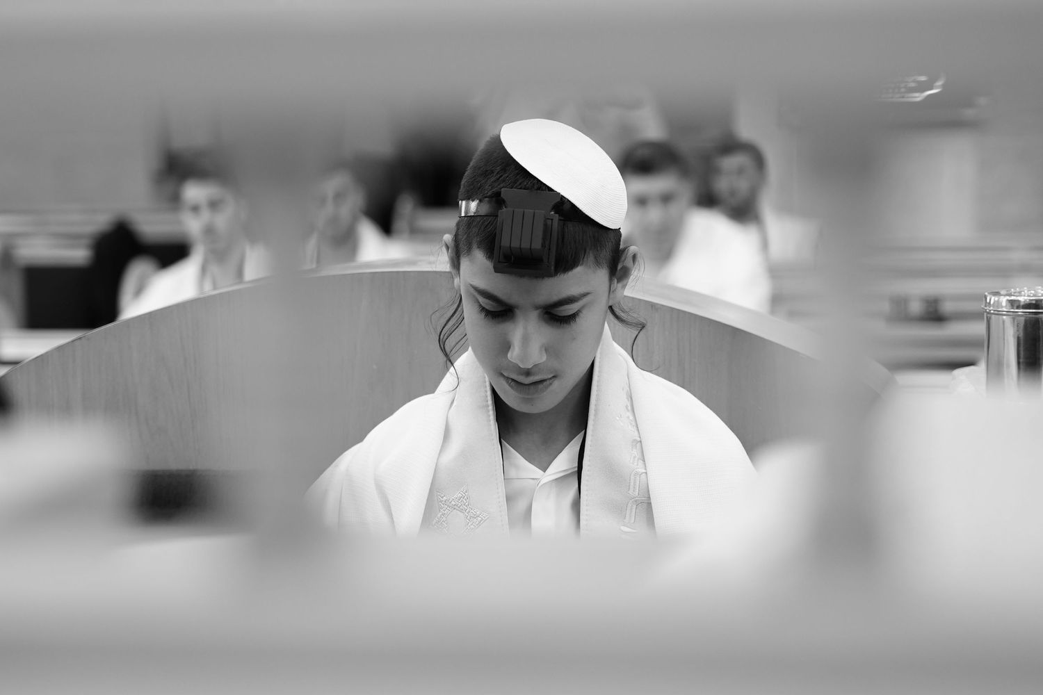Young Jewish boy wearing a kippah and tallit praying during his Bar Mitzvah ceremony in black and white.