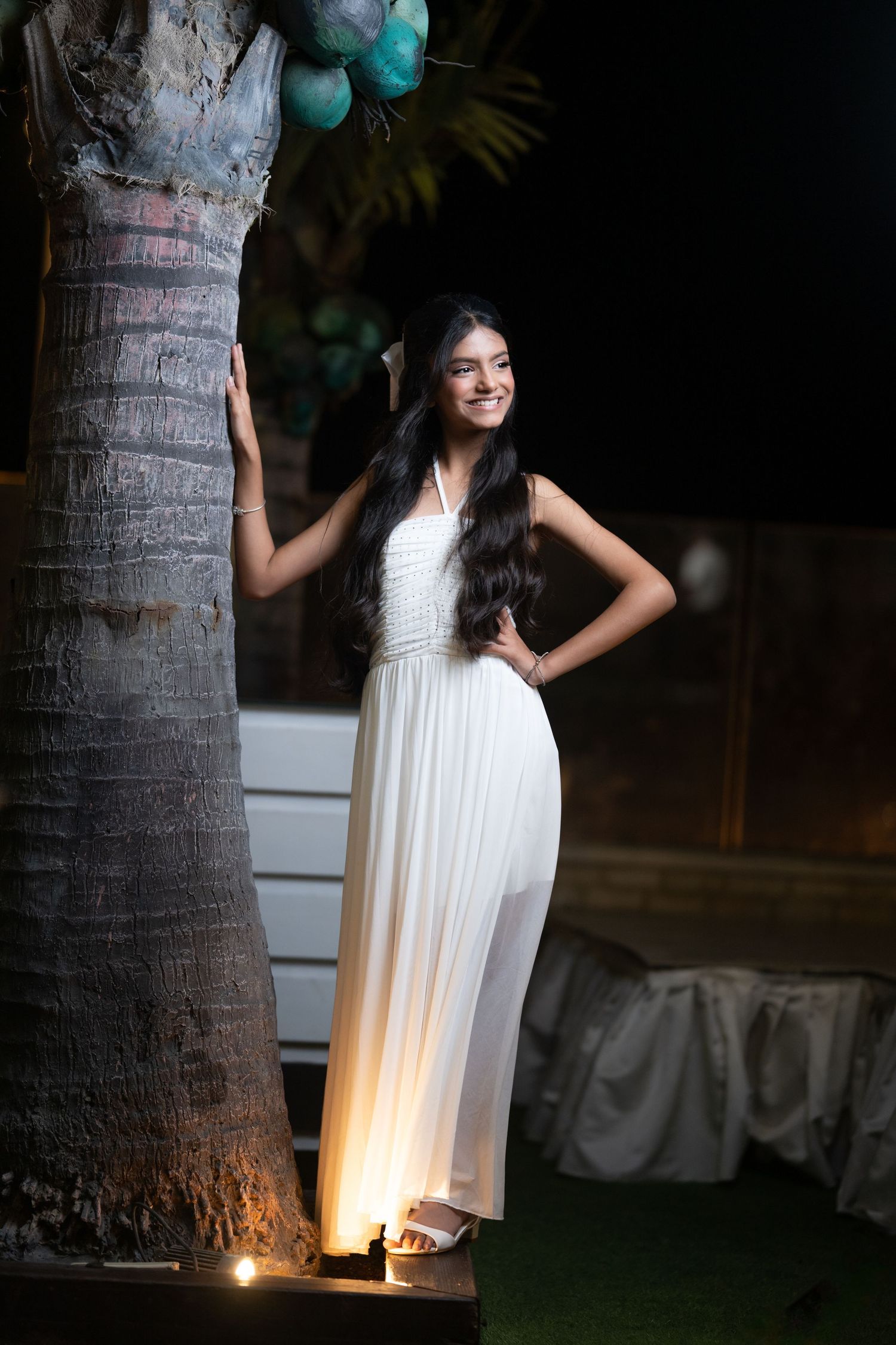A white dress illuminated by outdoor lighting near palm trees at night.