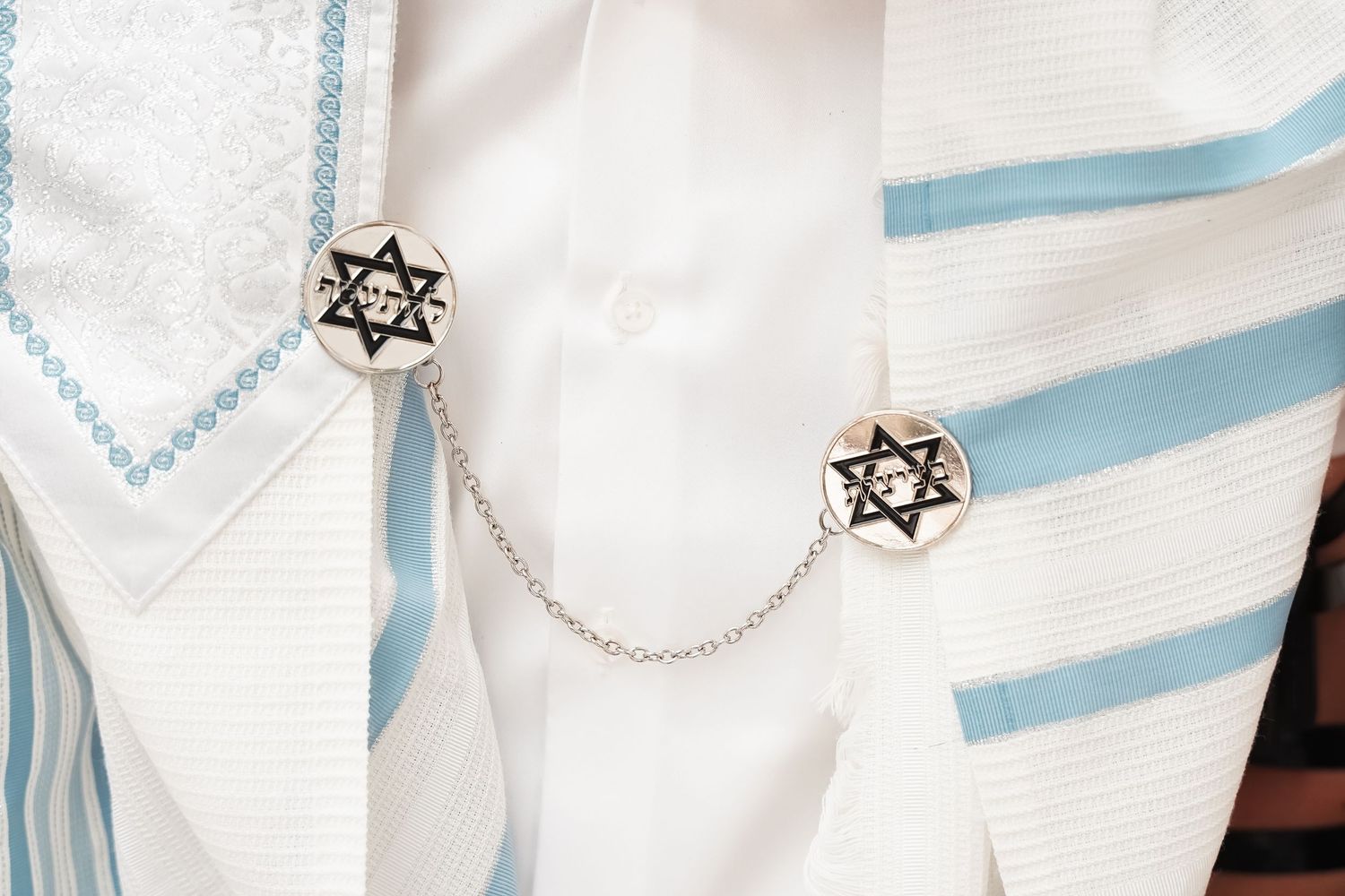White prayer shawl with blue stripes and Star of David decorations shown in detail.