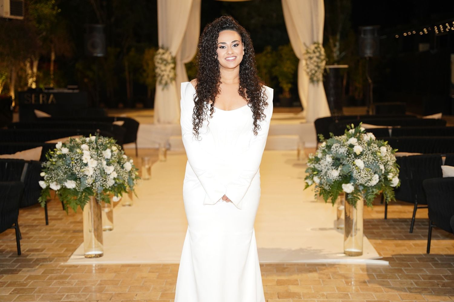 Wedding ceremony setup with white drapes and floral arrangements in elegant venue.