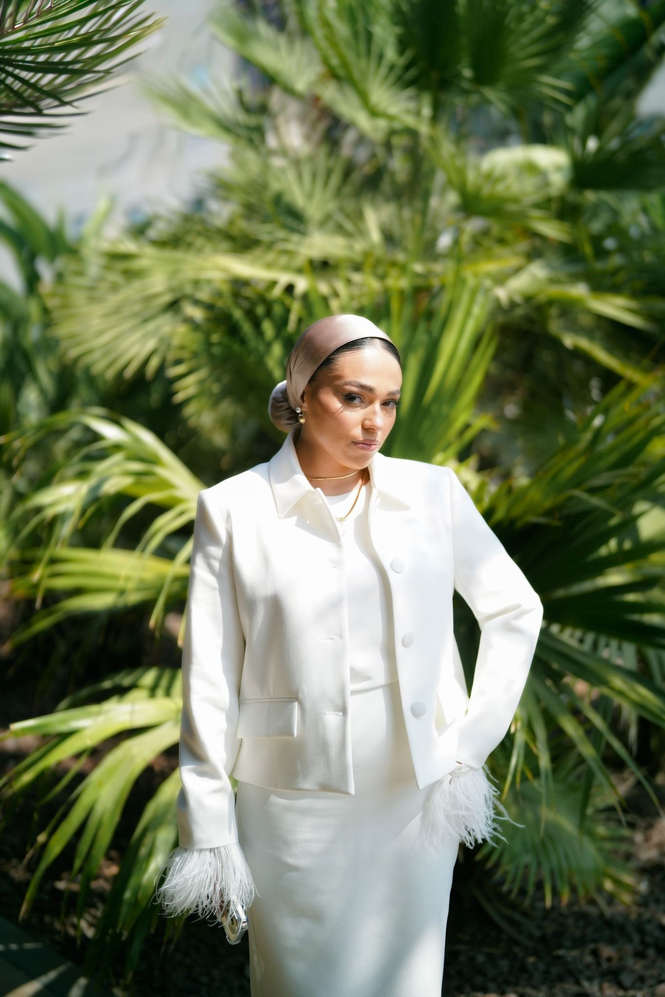 Elegant white suit with feather details against tropical palm background.