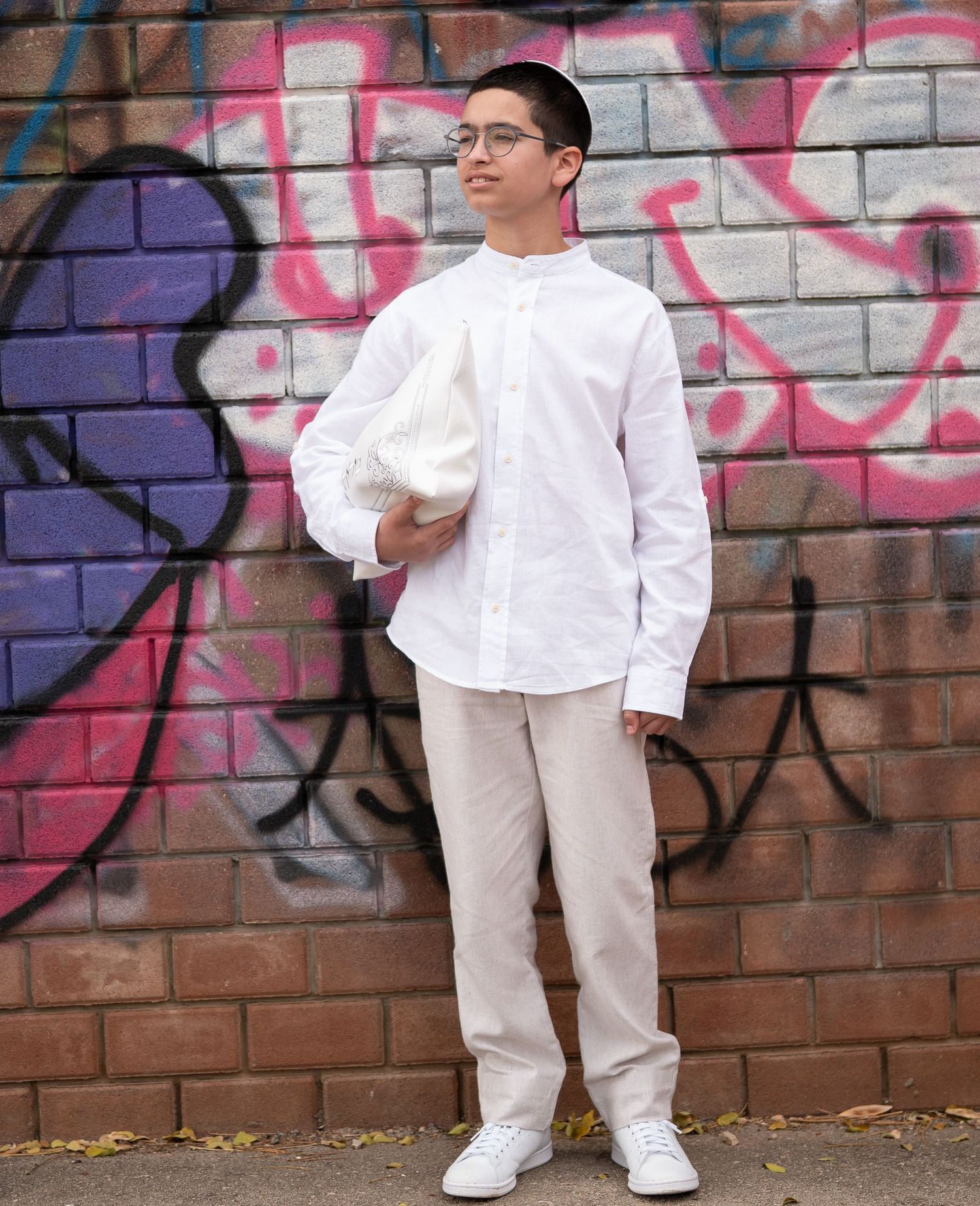 A full-length portrait against a brick wall decorated with pink and purple graffiti.