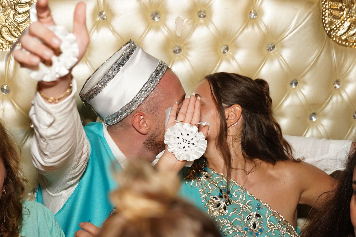 A celebratory moment at a wedding reception with guests in turquoise and white attire against an elegant tufted backdrop.