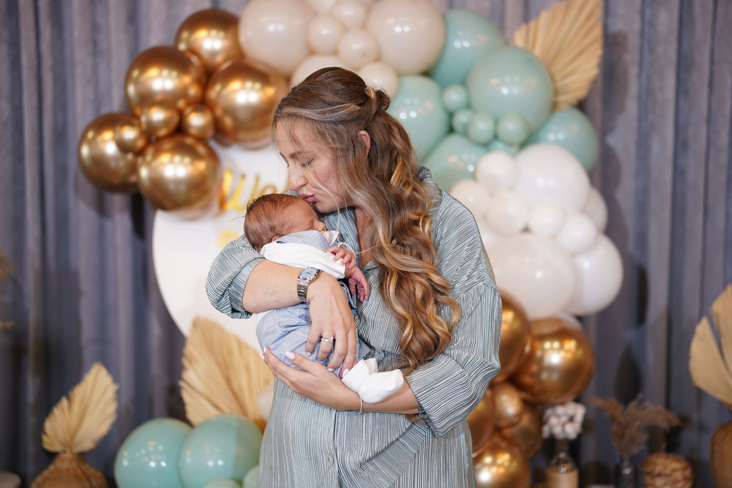 Joyful celebration at a baby shower with gold and mint balloon arch backdrop.