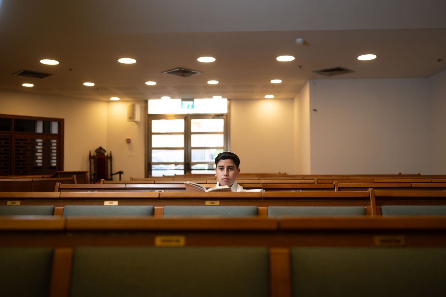 Interior view of modern synagogue sanctuary with wooden pews and recessed lighting.
