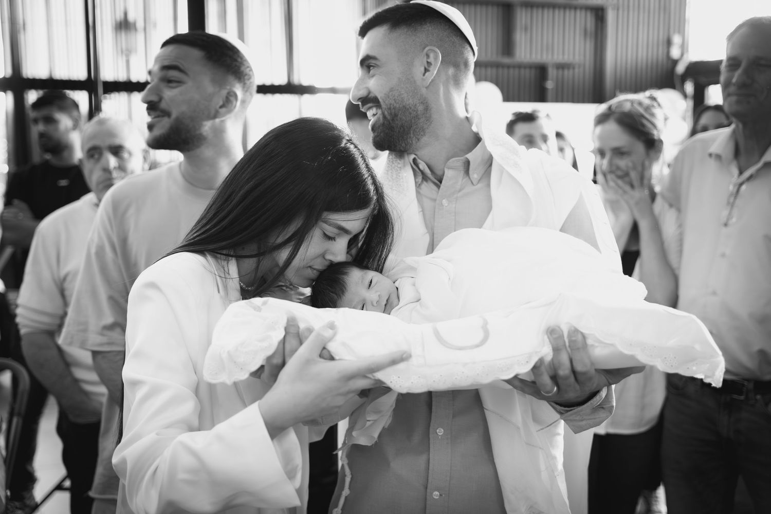 A black and white photo of parents sharing a tender moment with their newborn baby.