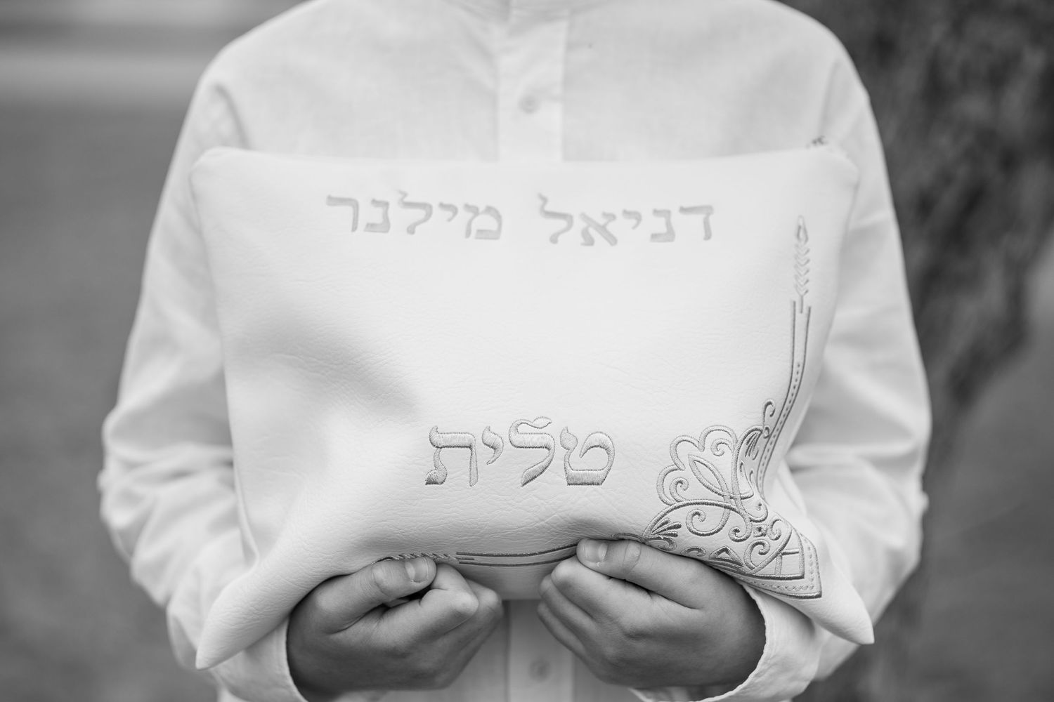 A white tallit with Hebrew text embroidered in traditional Jewish style.