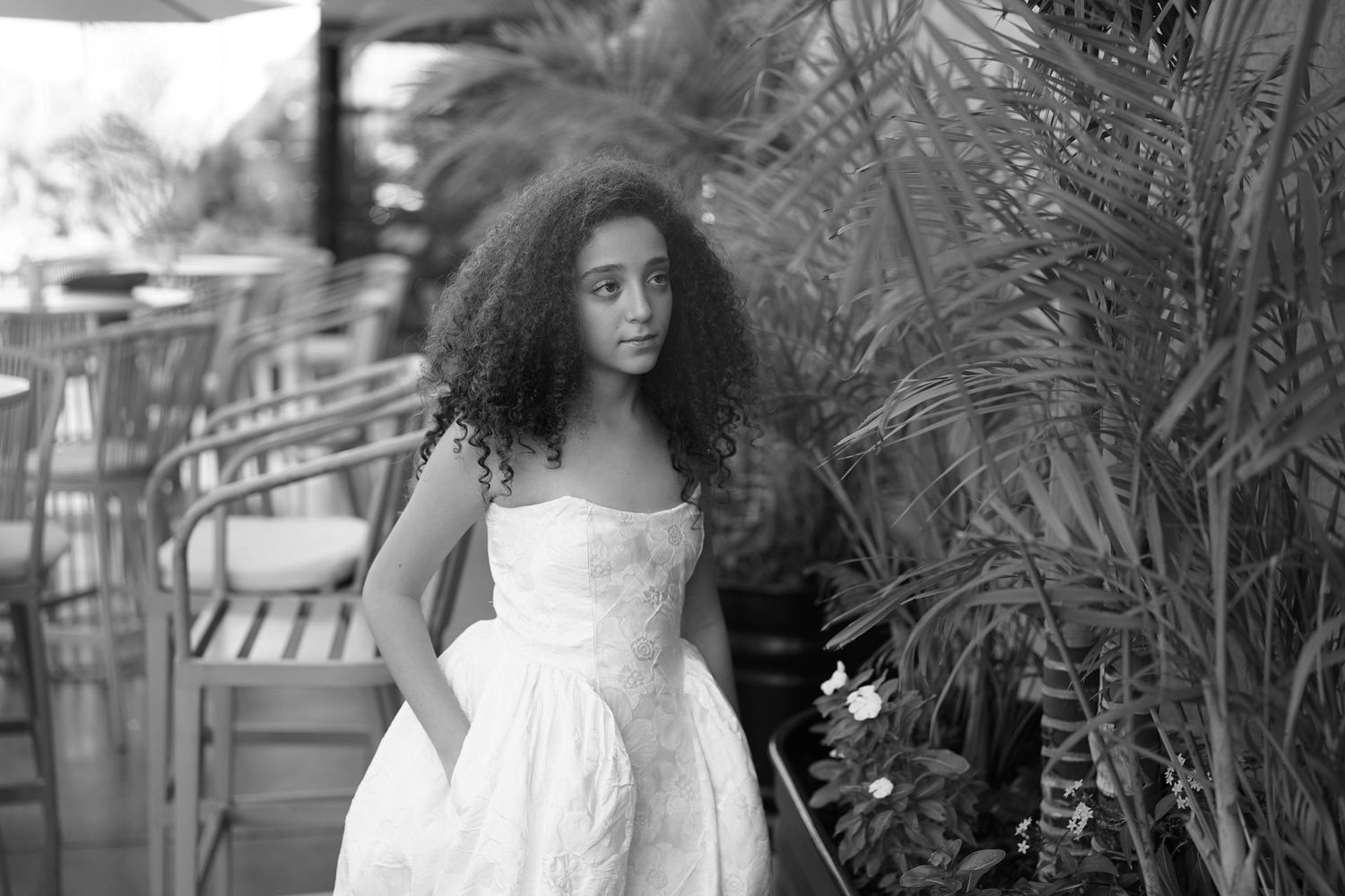Woman with curly hair poses in white dress outdoors.