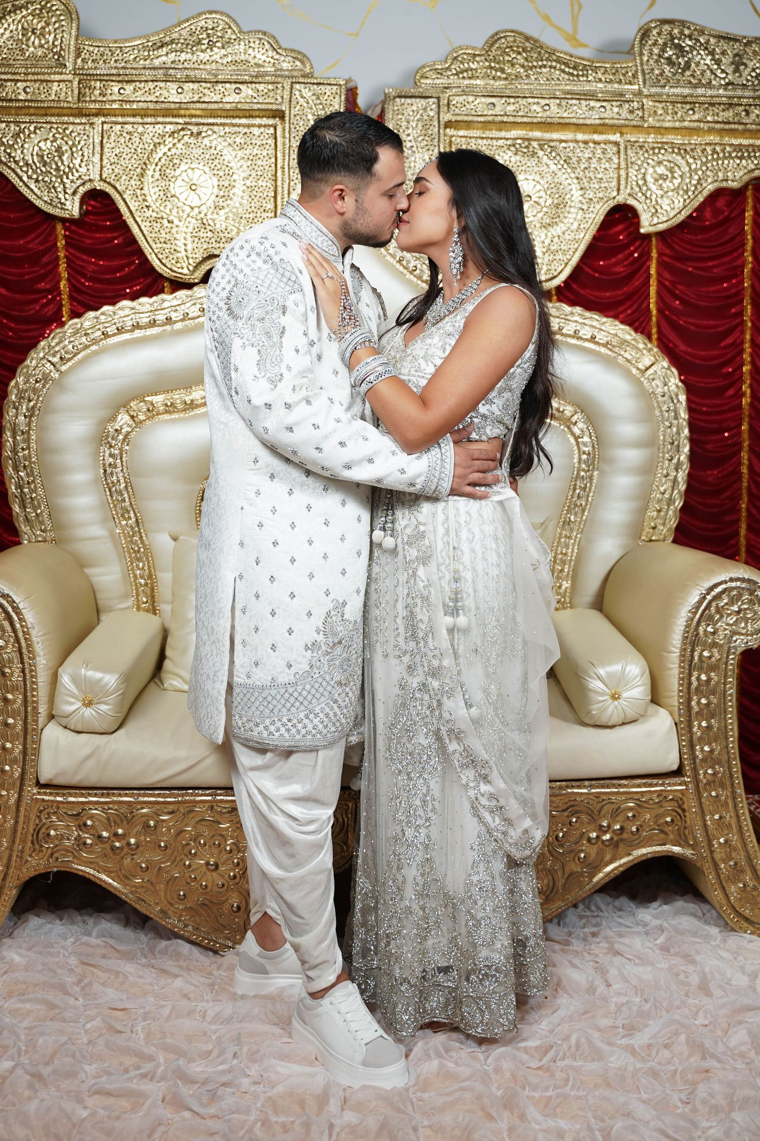 Ornate gold throne seating with red velvet backdrop in luxurious wedding setting.
