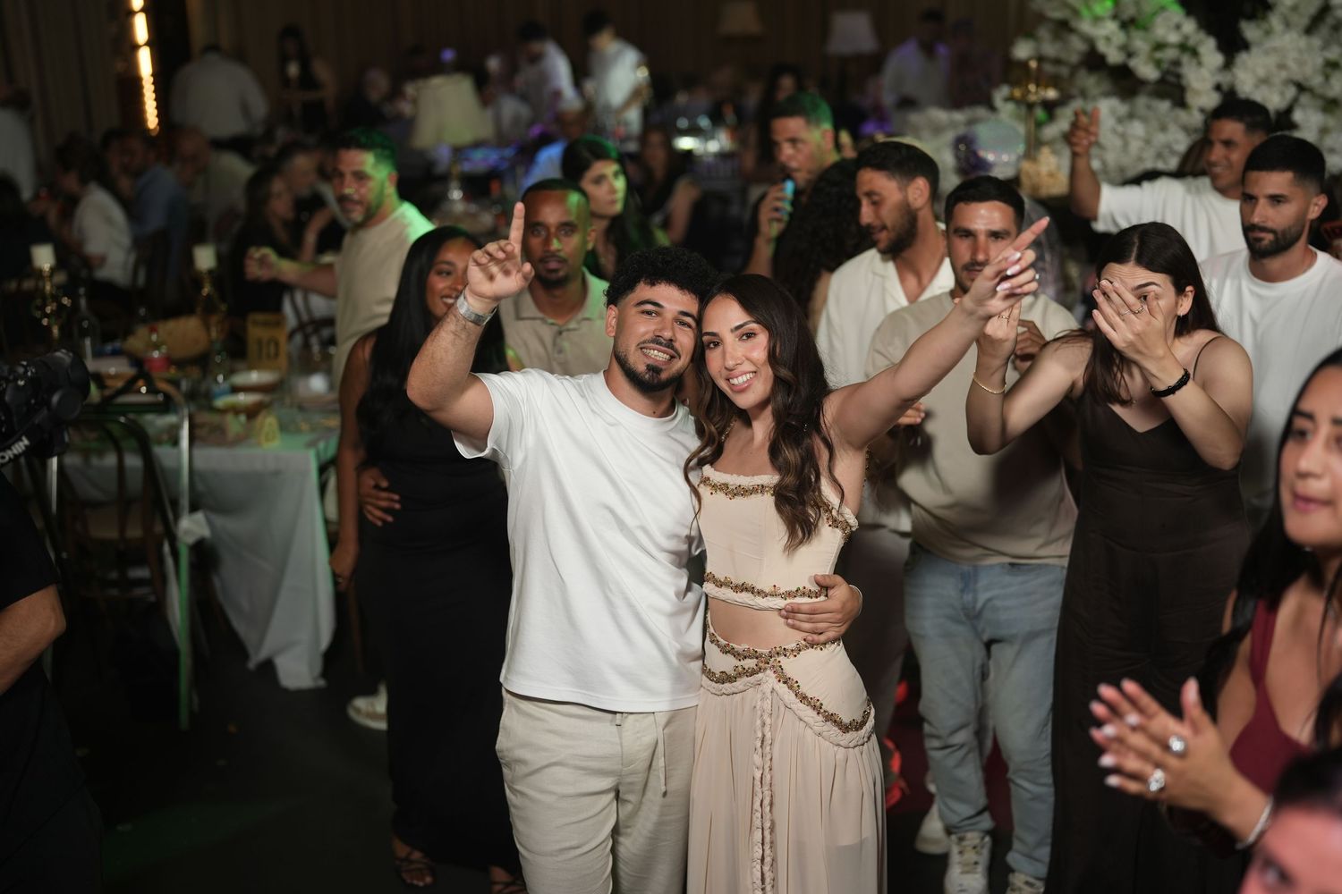 Couple smiling and dancing together at a lively indoor party event with guests celebrating in the background.