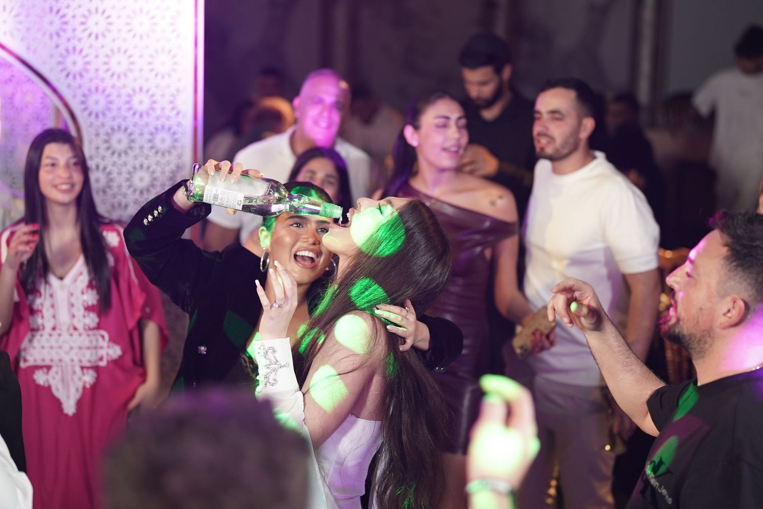 People dancing and celebrating at a nightclub with colorful lighting and party atmosphere.
