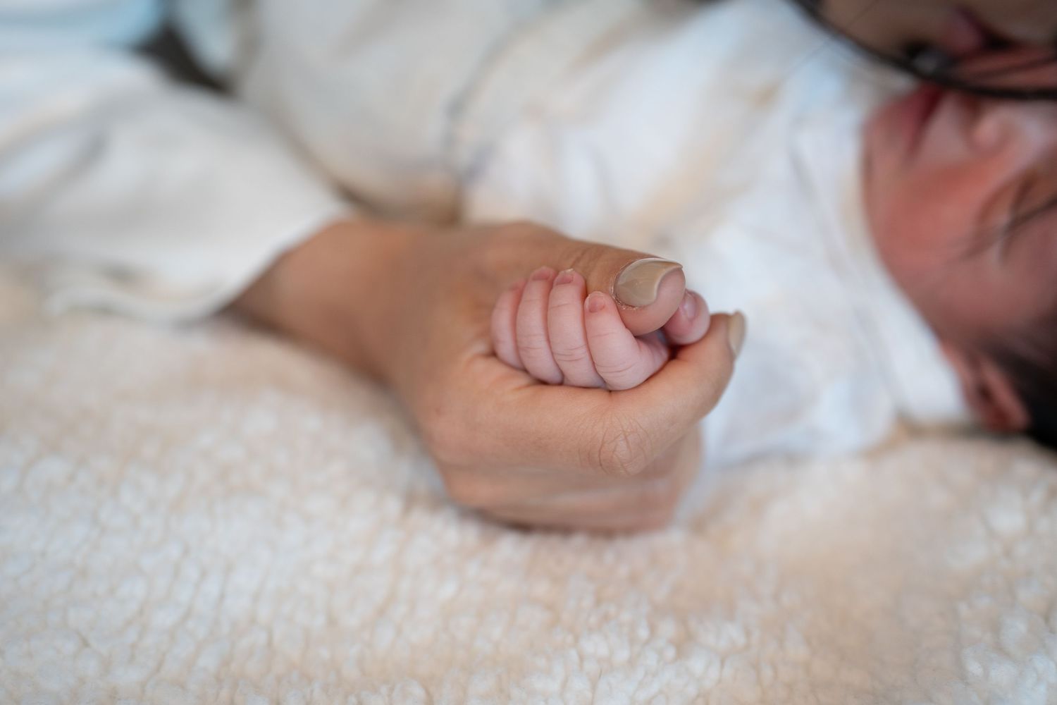 Close-up shot of a newborn baby's tiny hand grasping against white fabric.