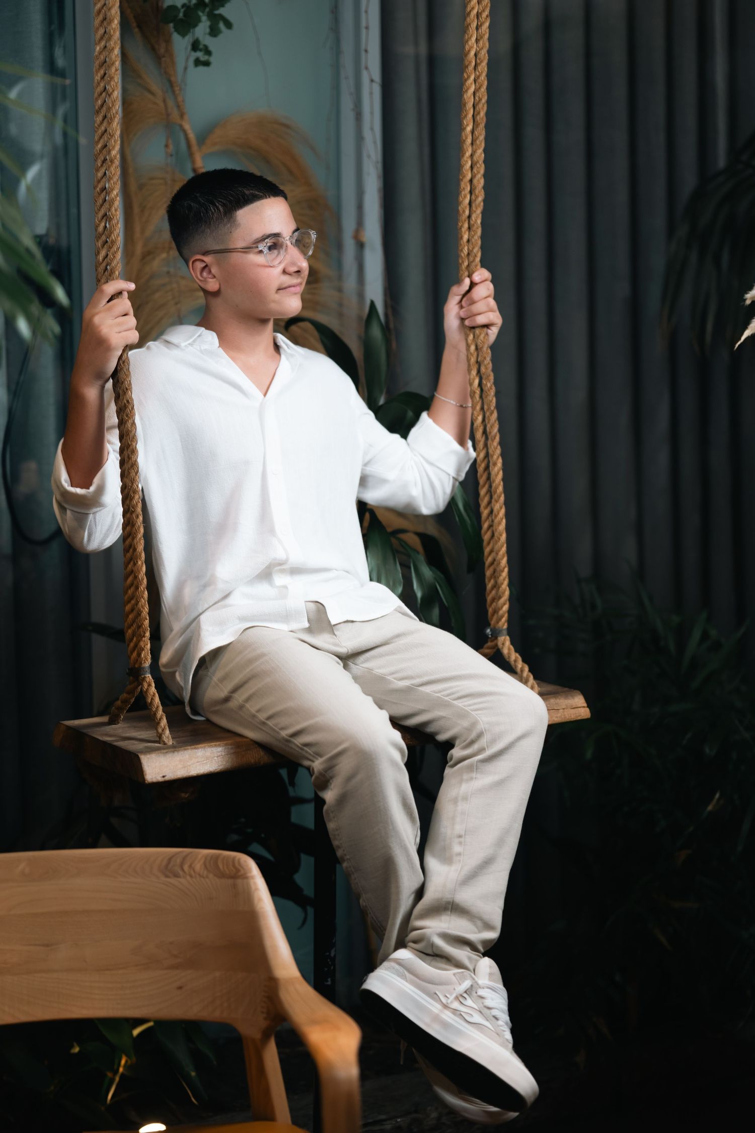 Person sitting on wooden rope swing in stylish indoor setting with plants.