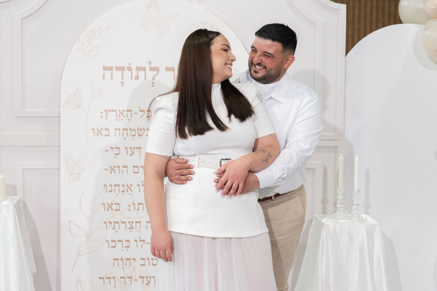 Intimate family photoshoot with white attire and decorative Hebrew text elements.