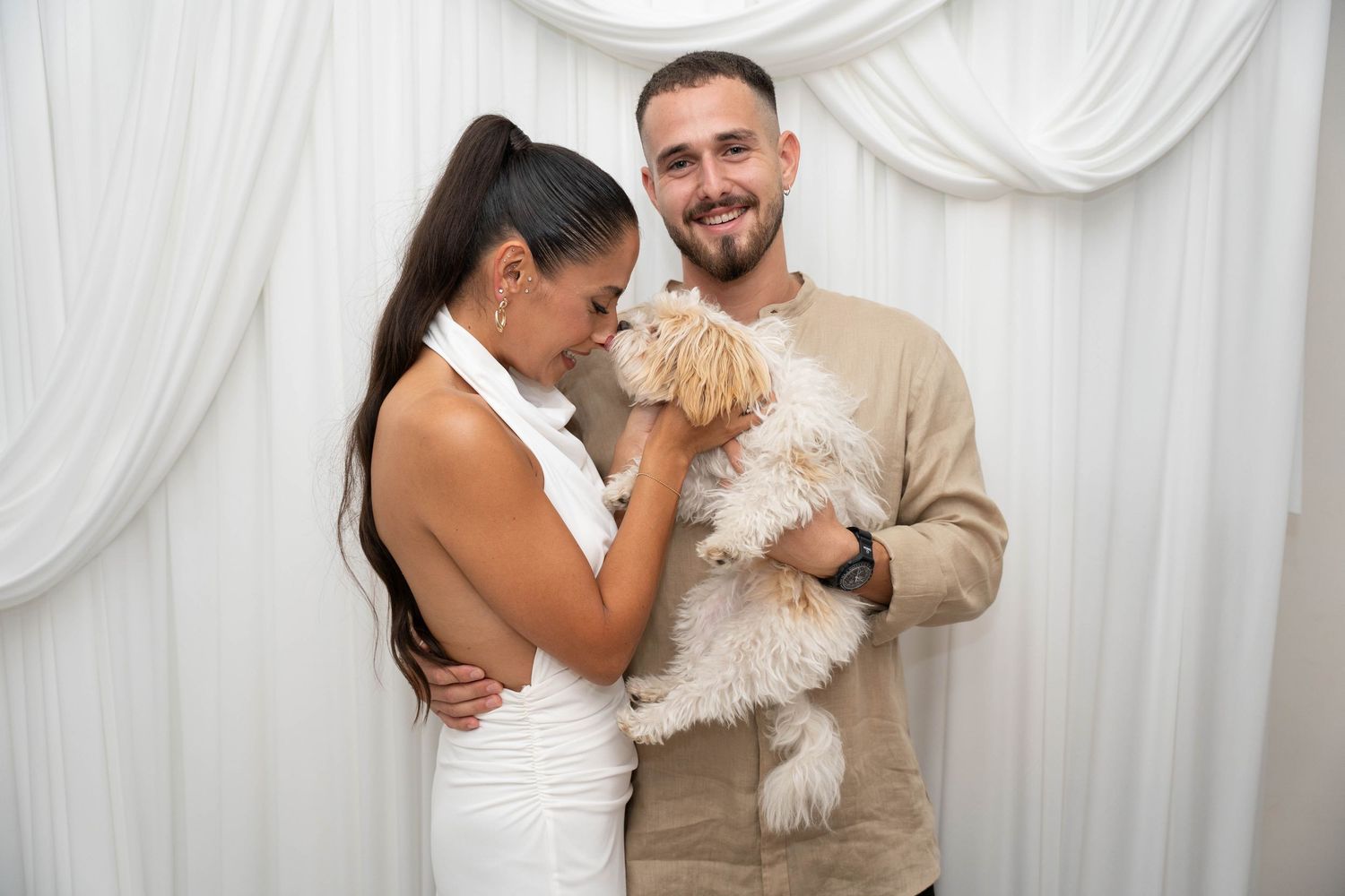 Couple with small white dog sharing joyful moment against white backdrop.