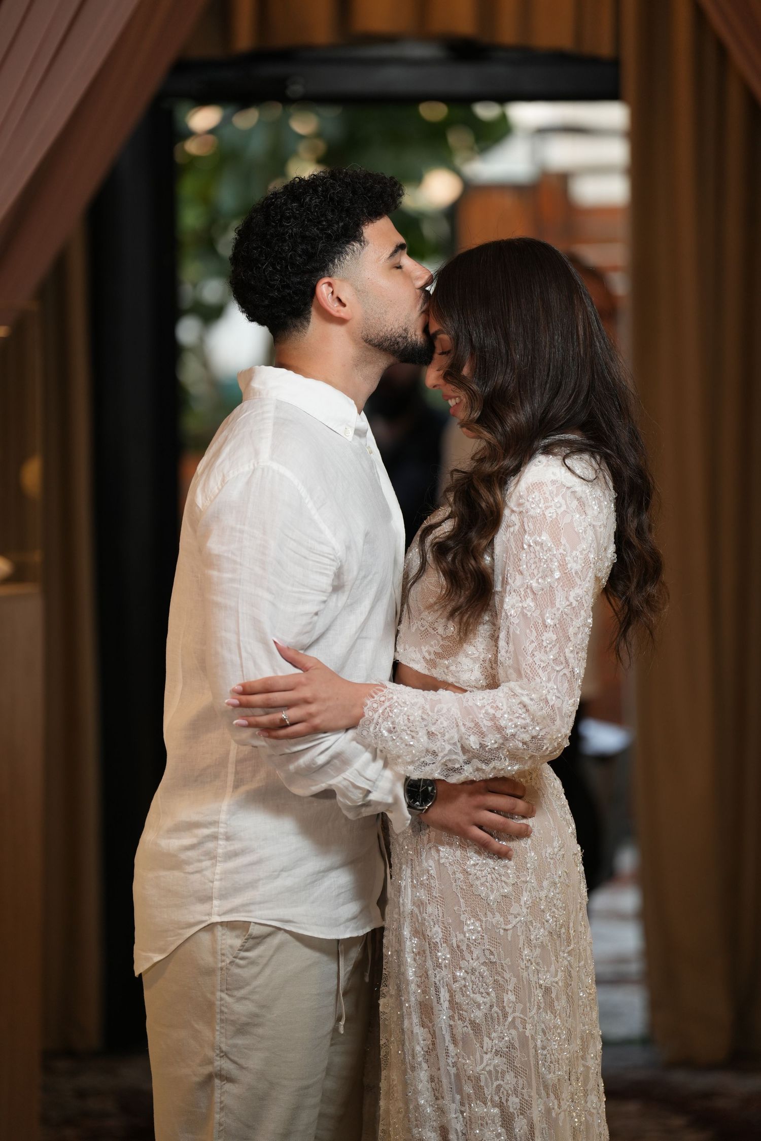 Couple sharing a romantic kiss at a wedding venue, dressed in white lace and cream attire.