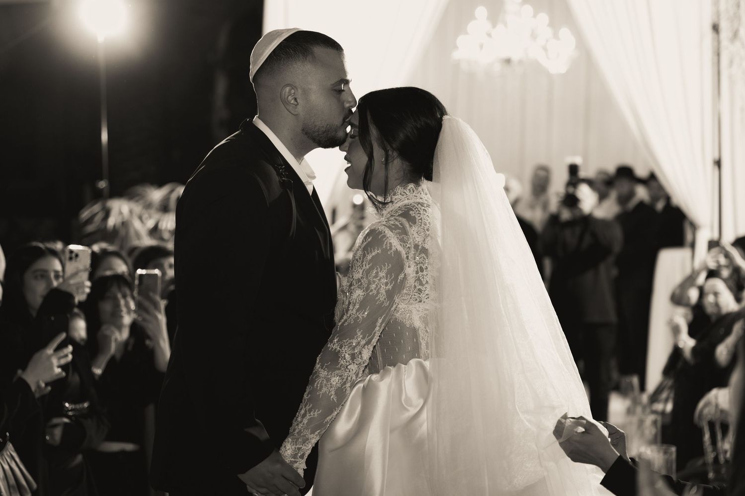 Black and white photo of a couple sharing a first kiss at their elegant wedding ceremony.