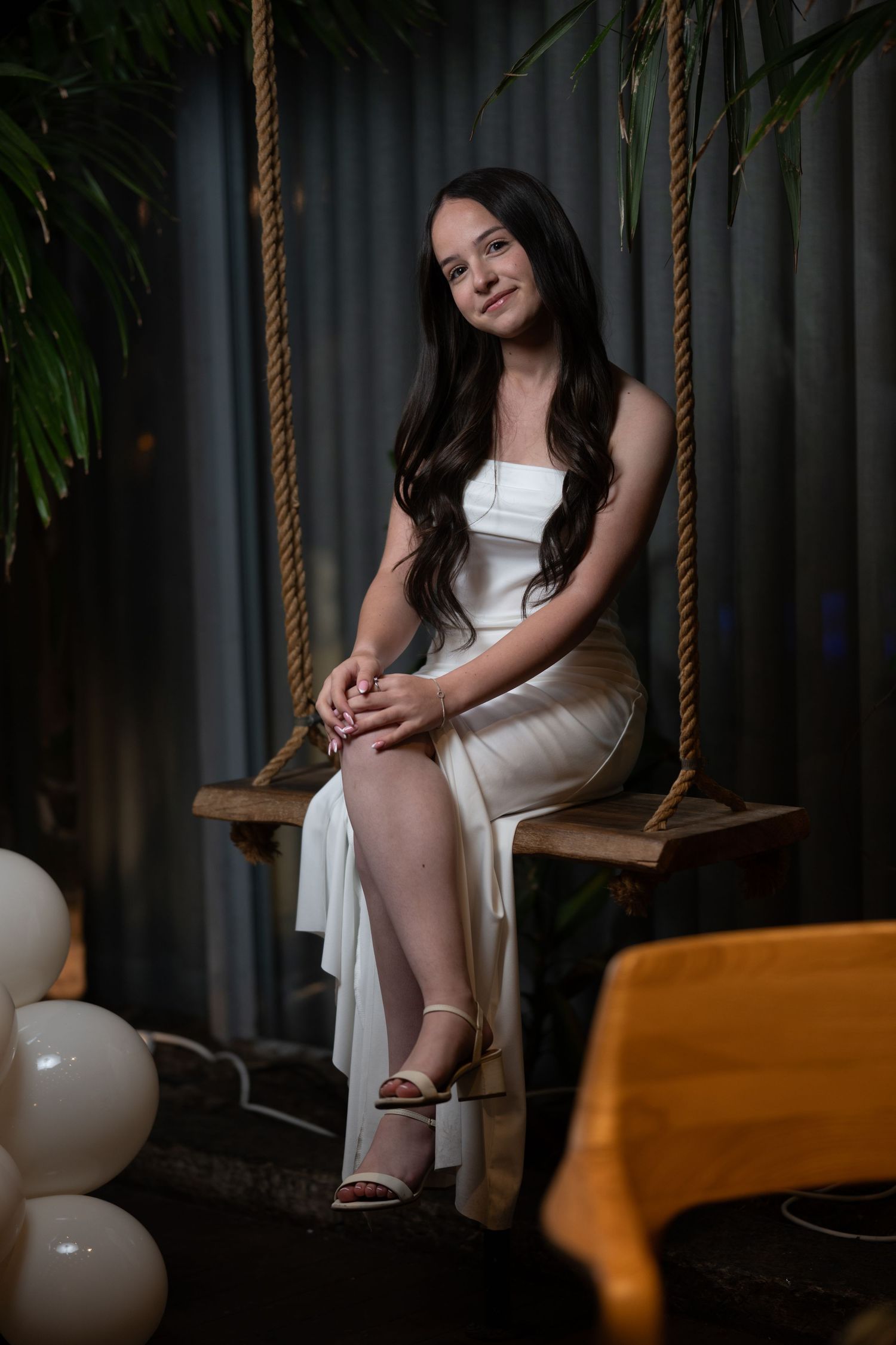 Elegant portrait session on wooden swing with white balloons and moody lighting.