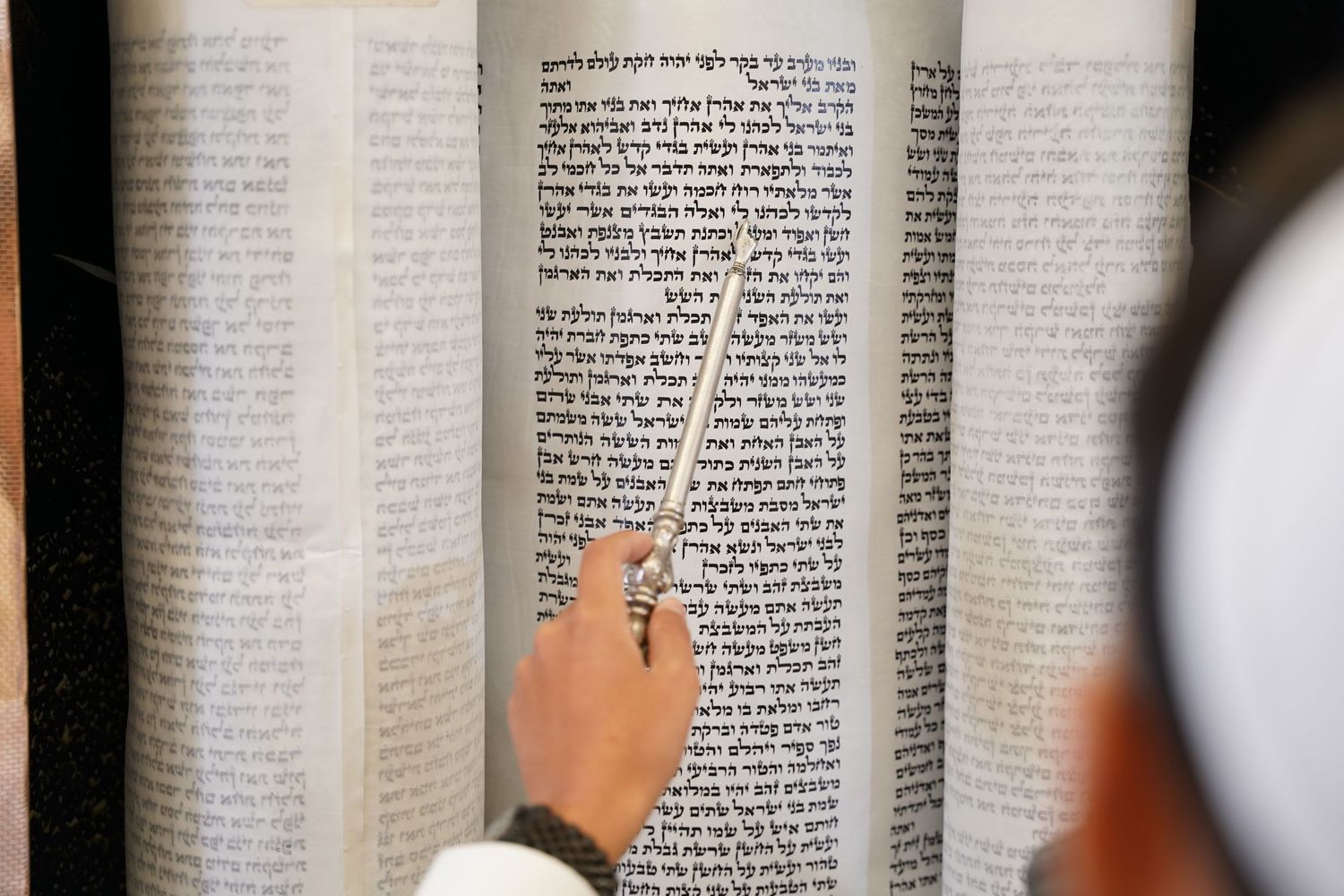 Close-up view of fingers pointing to Hebrew text in an open book.