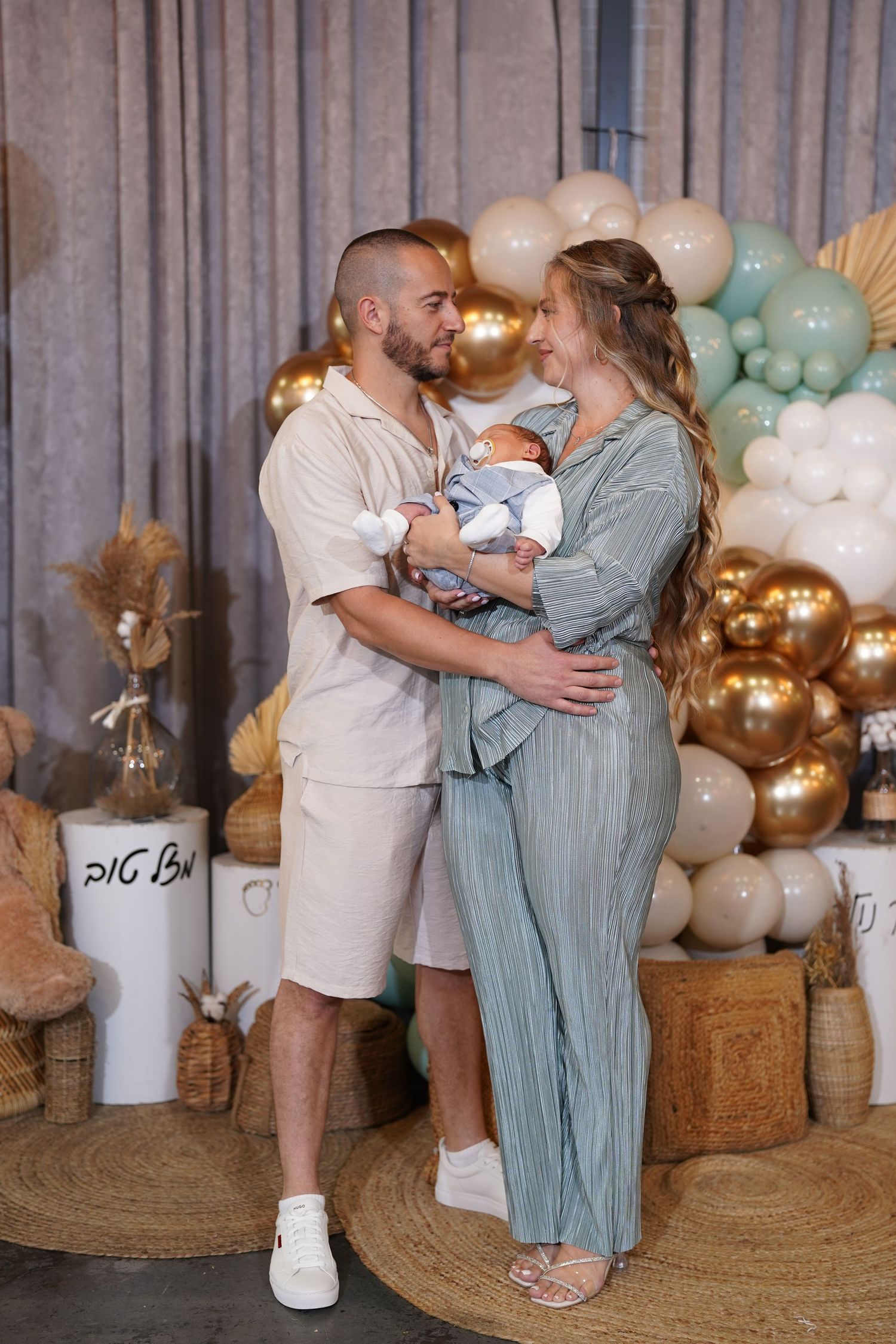 Family celebrates a special moment with hugs and kisses in front of gold and mint balloon decorations.