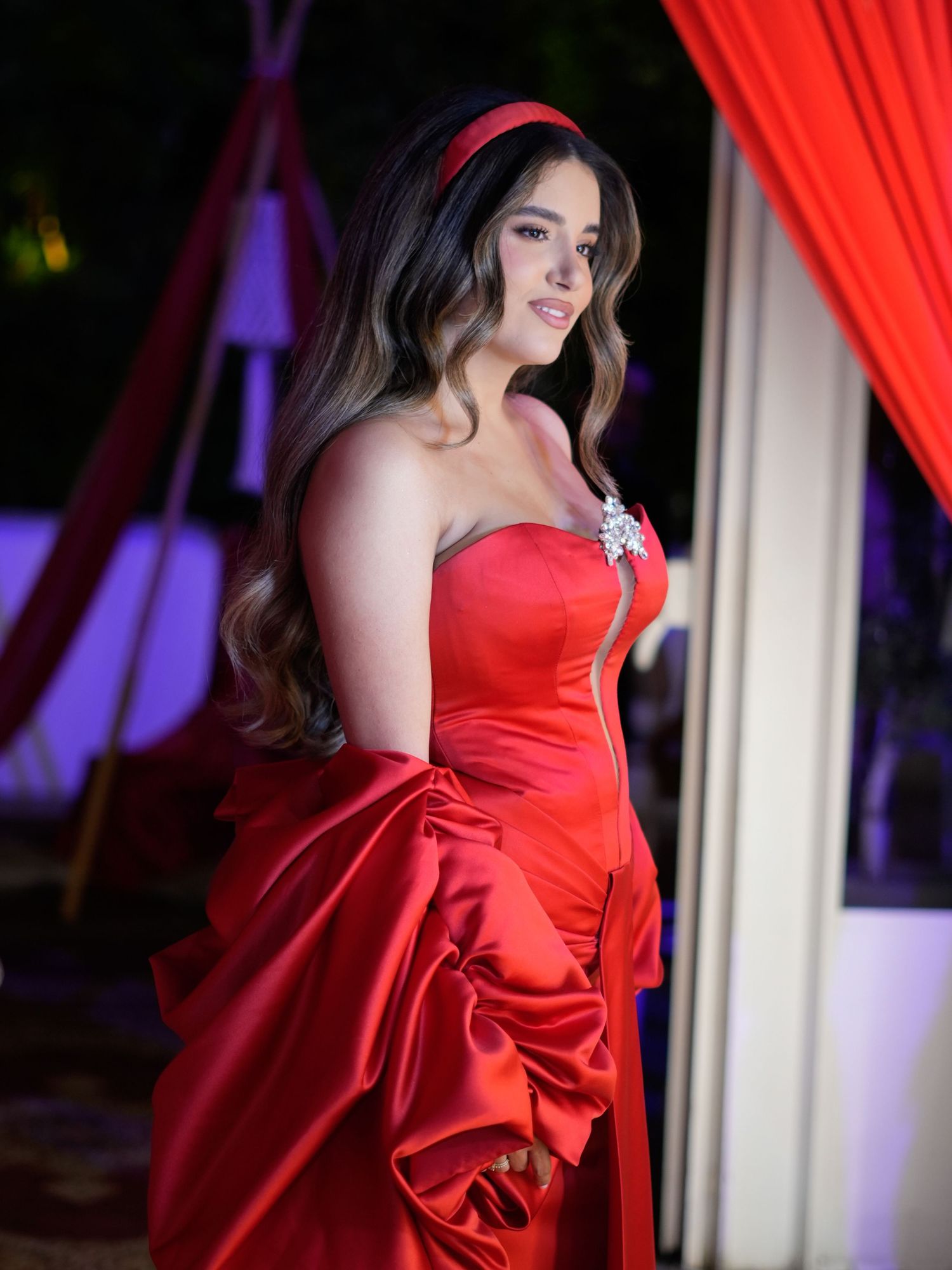 Dramatic fashion shoot with model in red evening gown against theatrical lighting.
