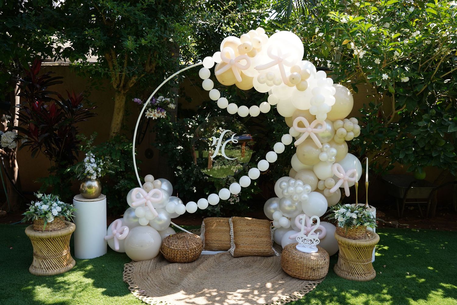 Elegant outdoor party setup with white and gold balloon arch decorations in a garden setting.
