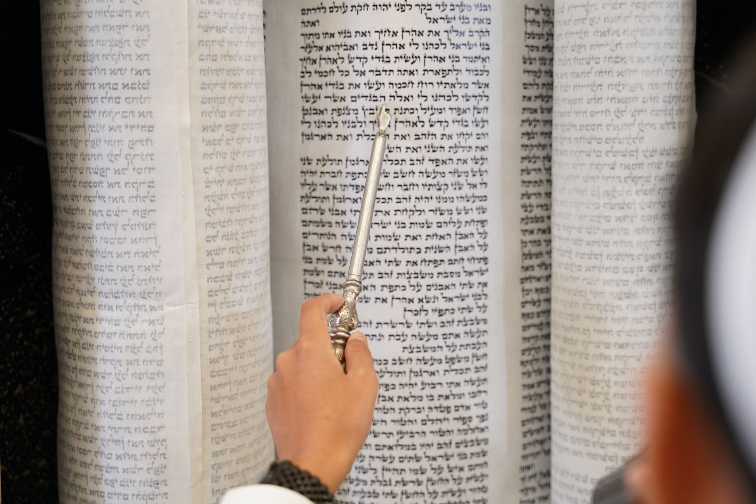 Close-up of hand pointing to text in religious scripture or holy book.