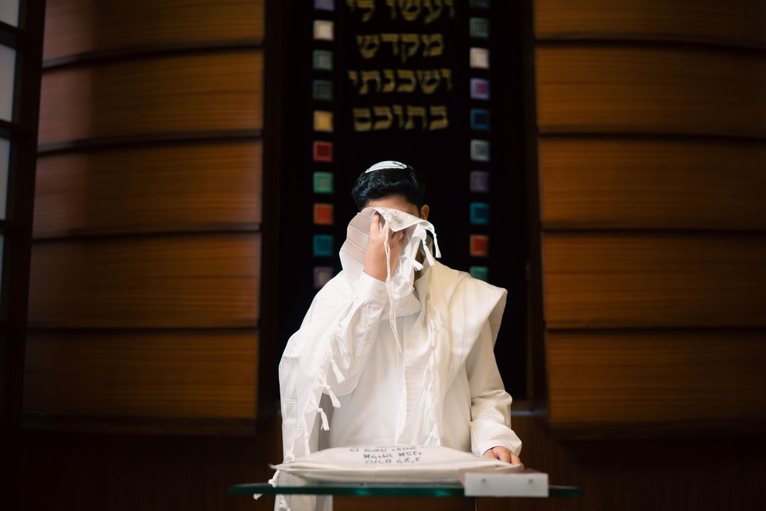 Religious ceremony with person in white garments blowing shofar near Hebrew text display.