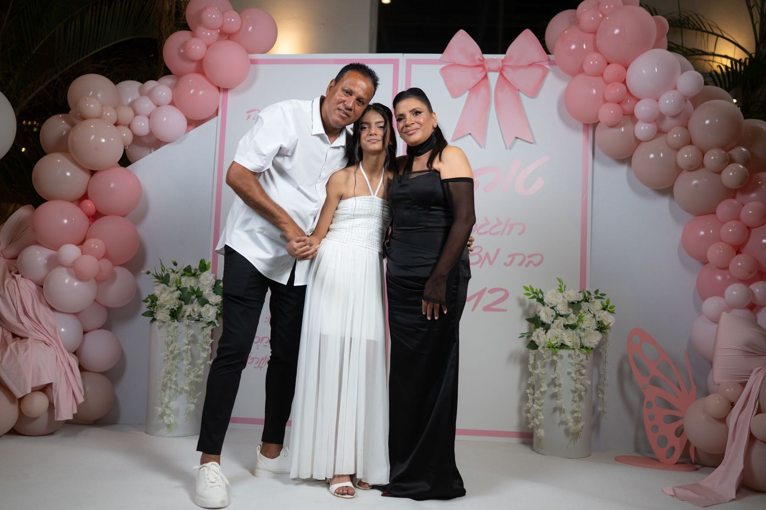 Elegant celebration setup with pink balloon arch decorations and white floral arrangements at an indoor venue.