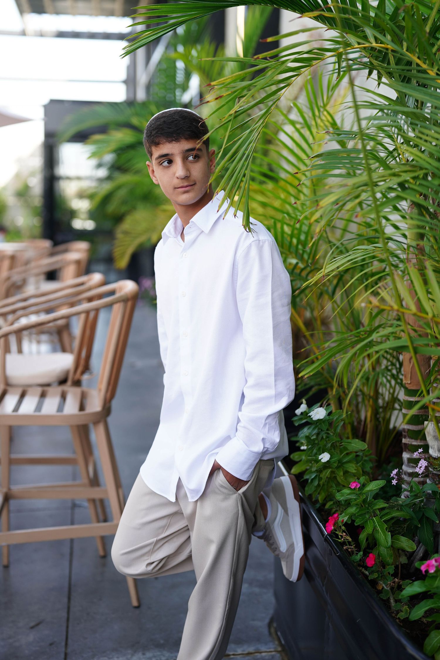 Person in white button-down shirt and khaki pants poses against tropical garden backdrop.