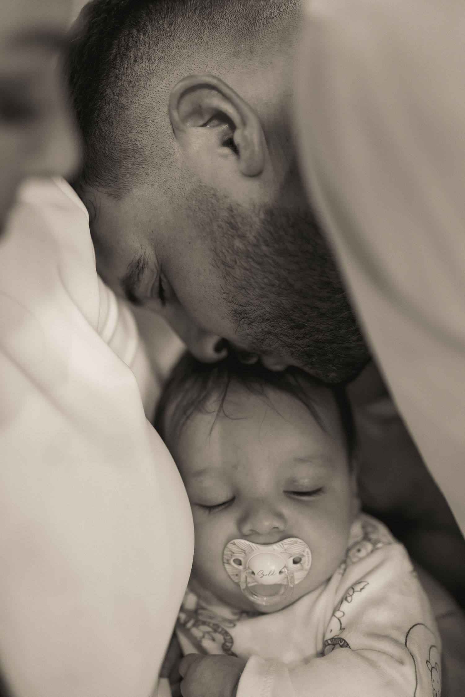 Tender black and white photos of a parent giving gentle kisses to a sleeping baby.