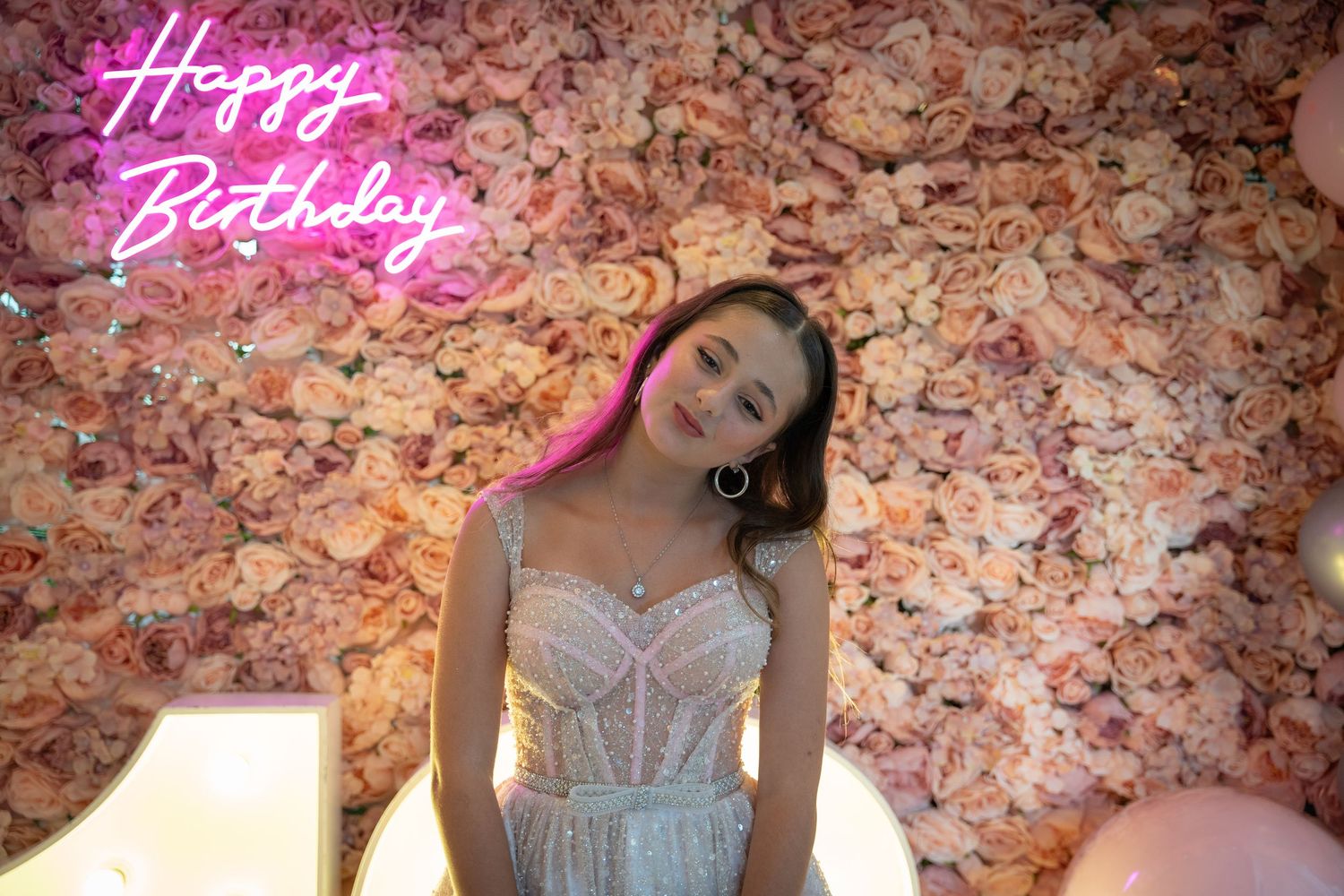 Elegant white dress photographed against pink floral wall with neon birthday sign.