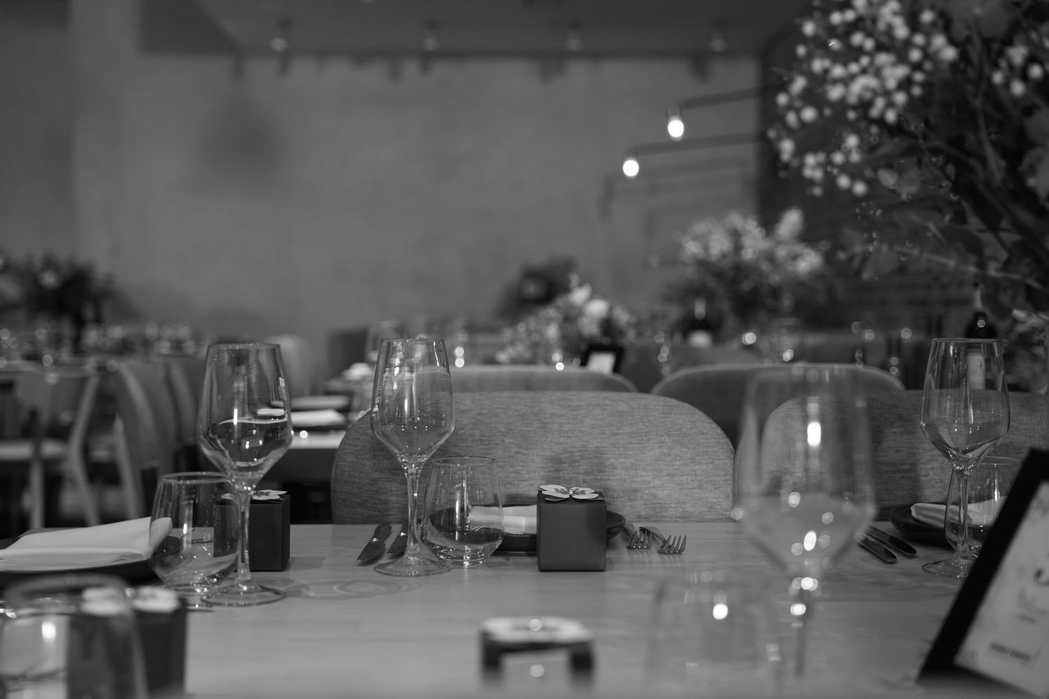 Elegant wedding reception table settings with glowing string lights in a dimly lit venue.