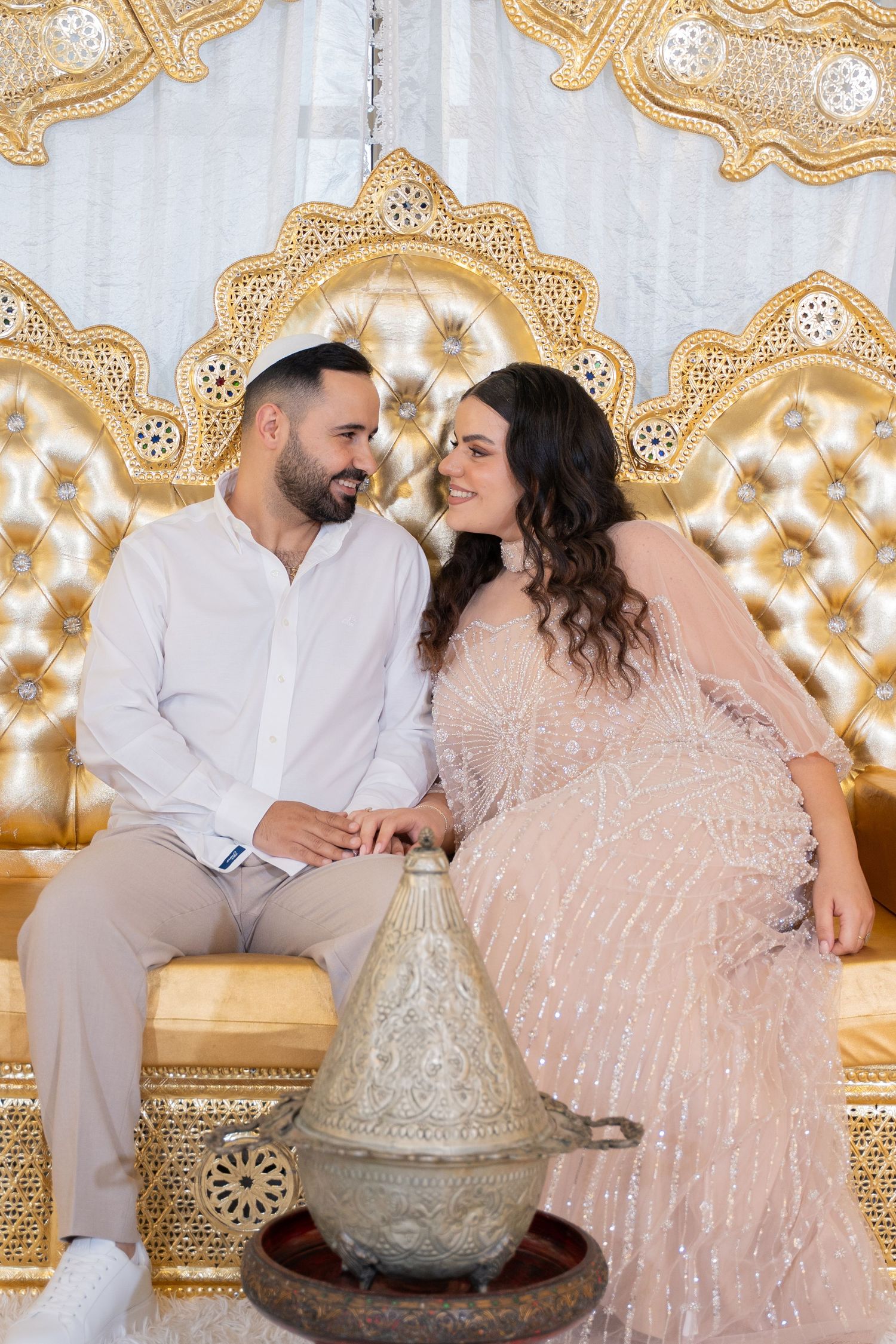 Couple shares romantic moment on luxurious gold tufted seating with decorative lantern.