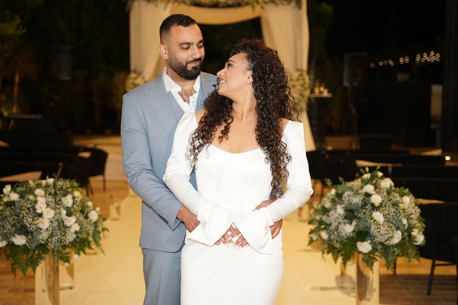 Wedding couple sharing a romantic moment under elegant floral decorations and warm lighting.