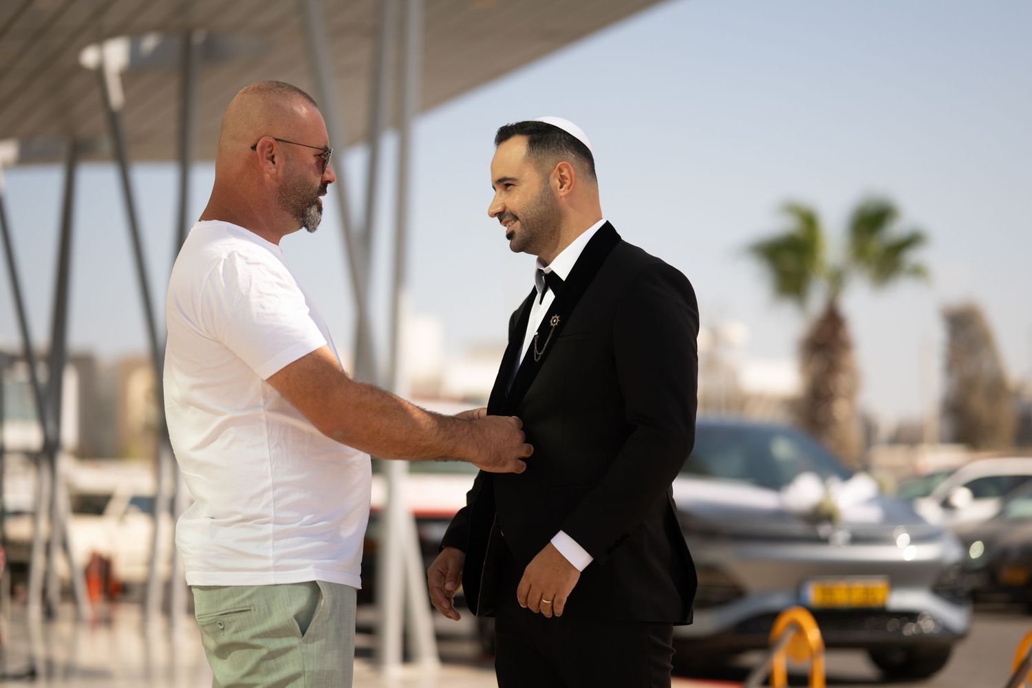 Two people having a conversation outdoors near a marina with palm trees in the background.