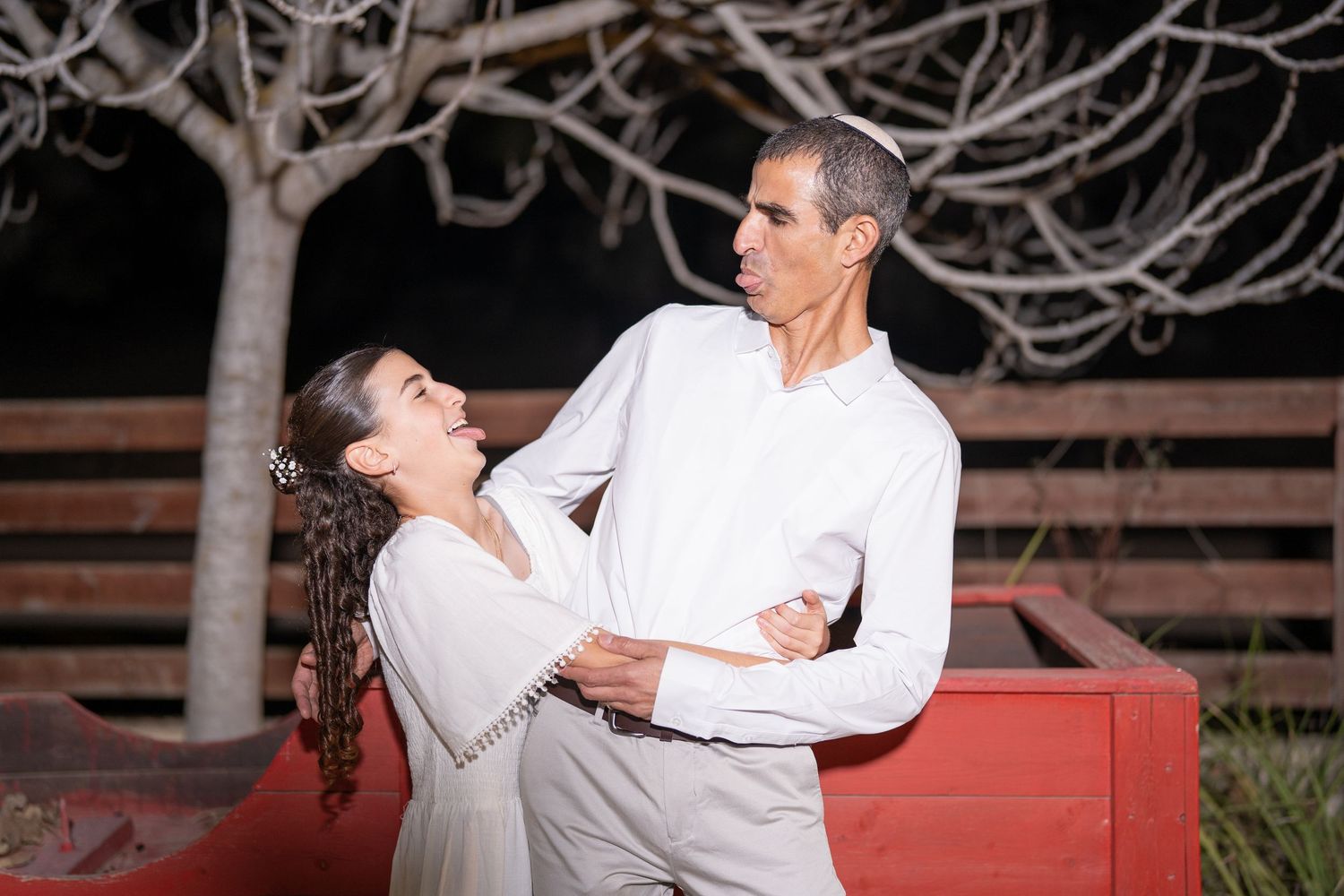 Two people in white shirts sharing an affectionate moment outdoors at night.