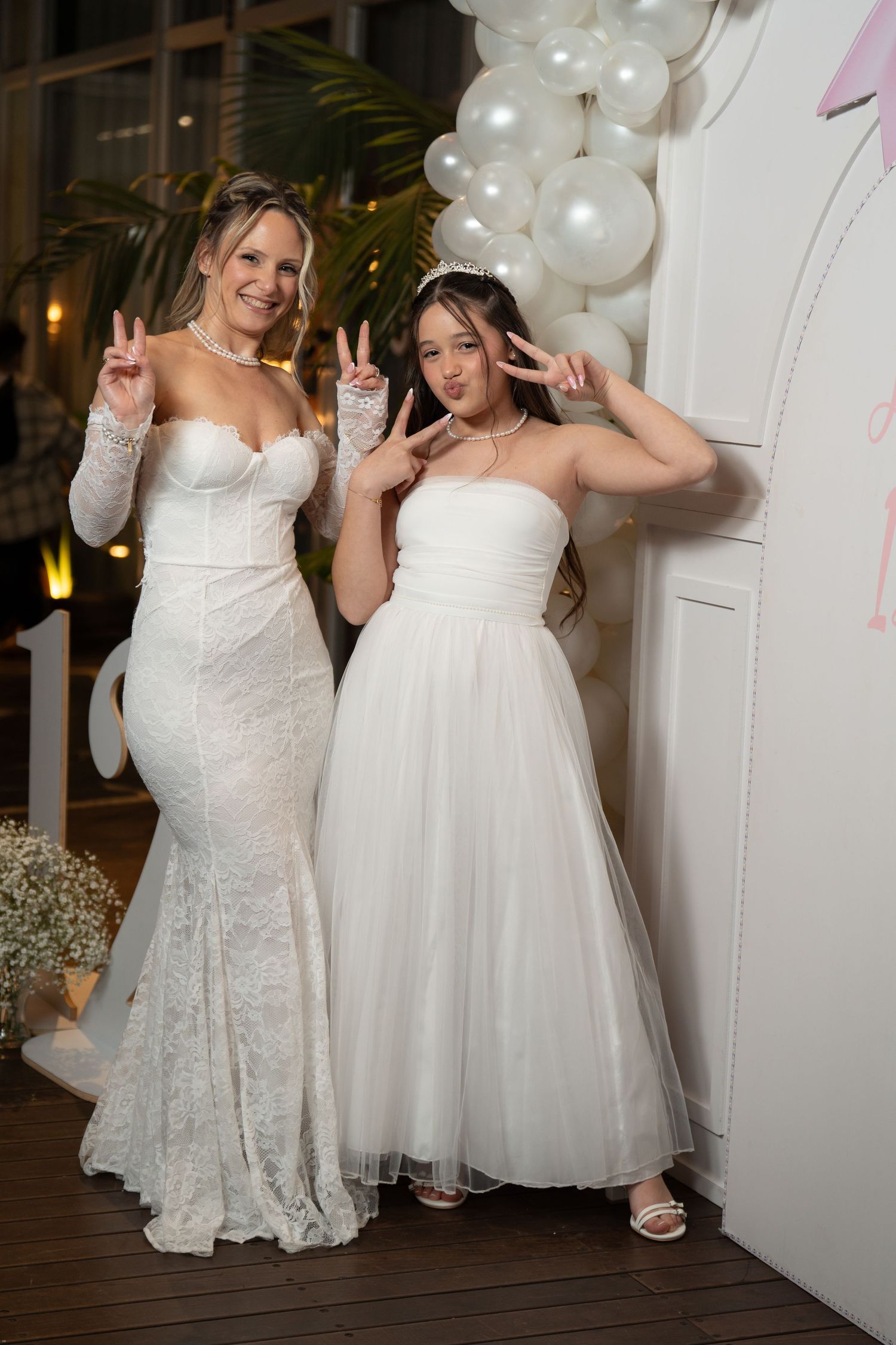 Two brides in white wedding dresses pose together with balloons in the background during their celebration.