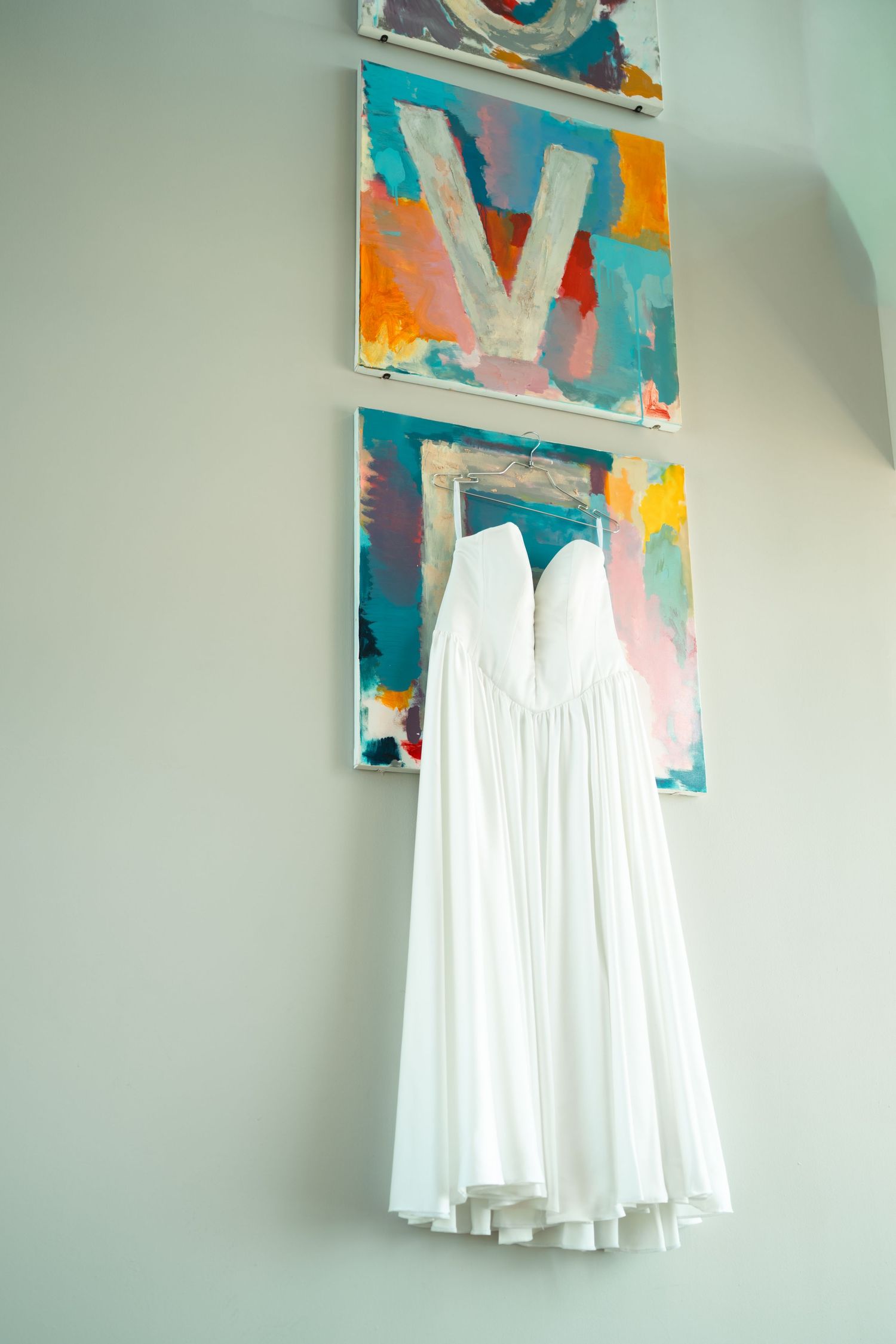 White wedding dress hanging against wall with colorful abstract artwork.