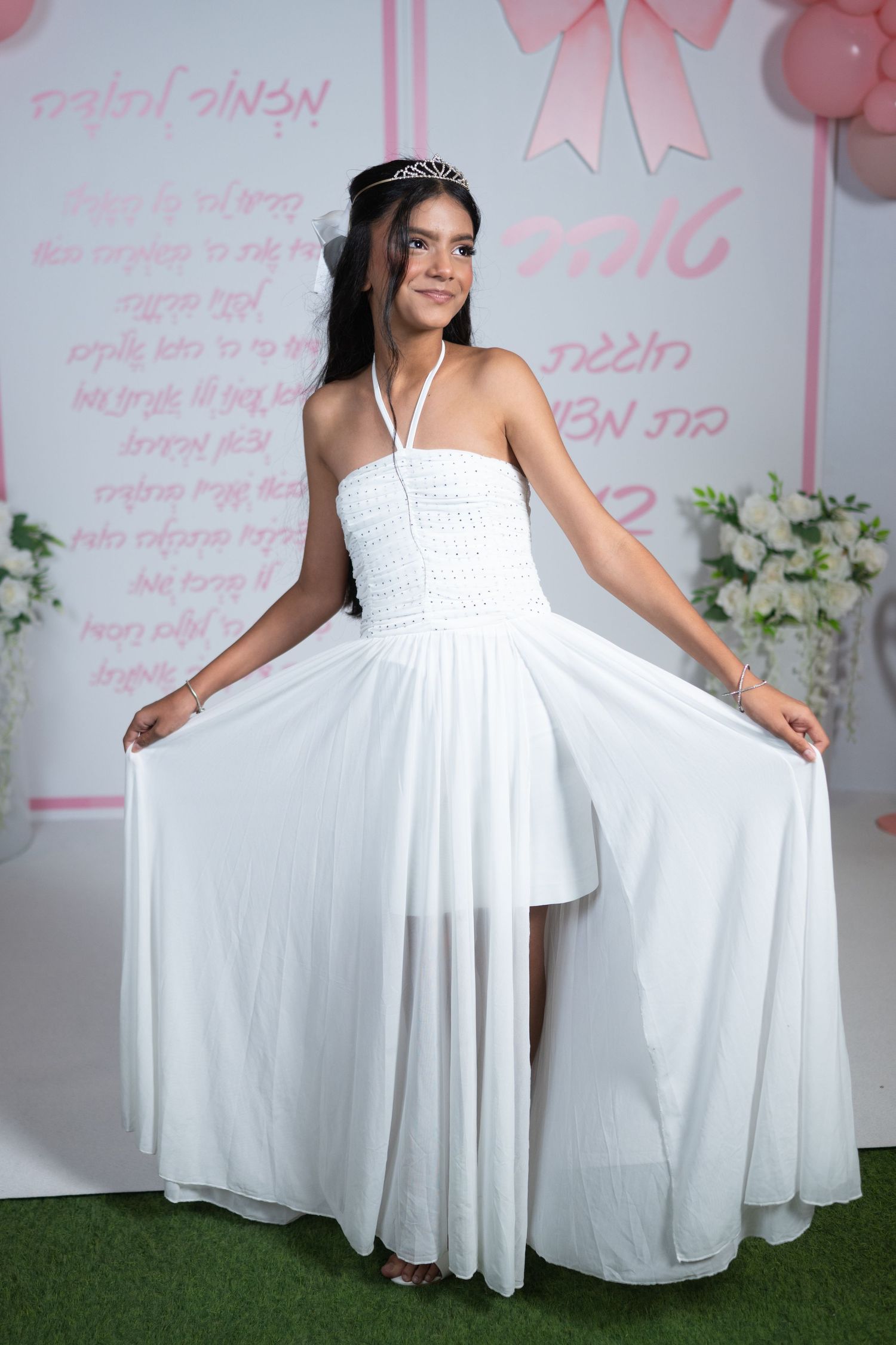A flowing white dress is showcased against a pink backdrop with balloon decorations.