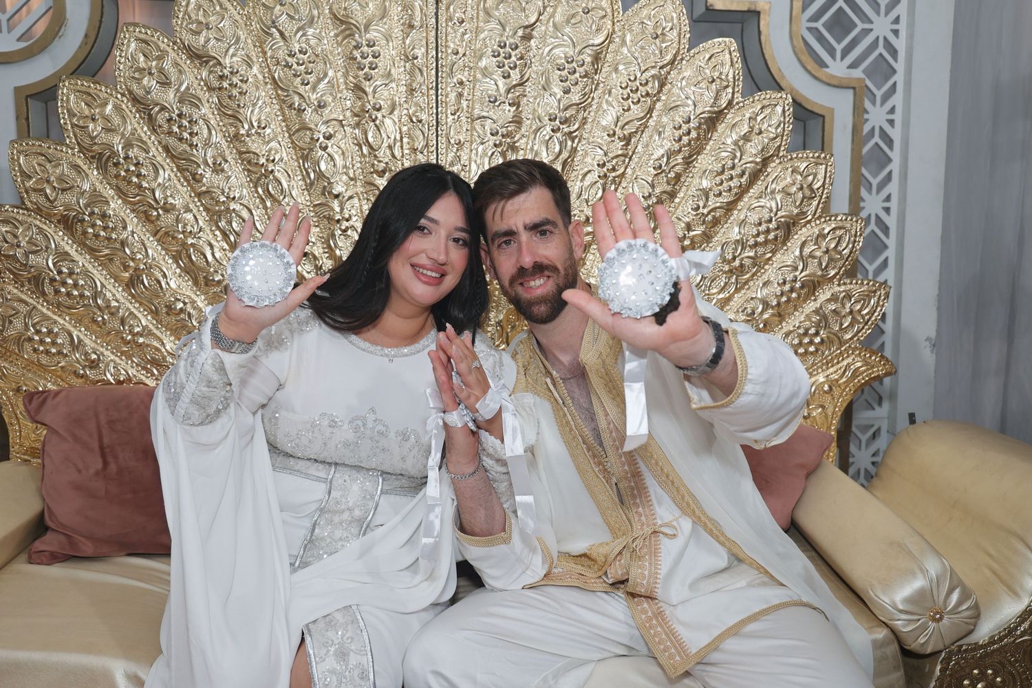 Luxurious wedding venue featuring gold sunburst wall decorations and elegant white seating arrangements.