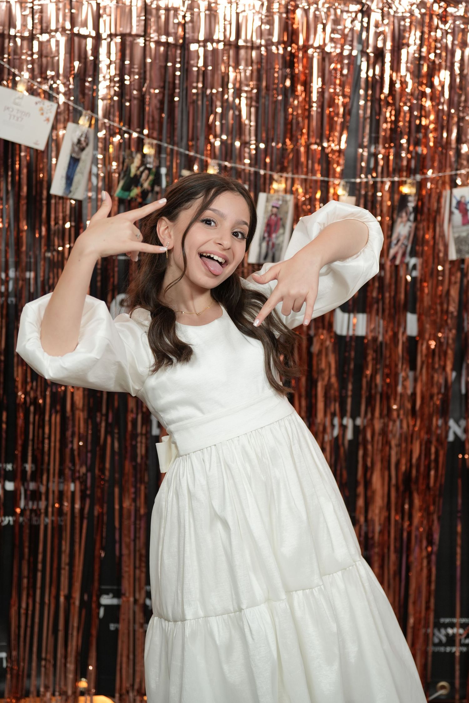 Woman in white dress poses playfully against a rose gold tinsel backdrop in a series of celebratory photos.
