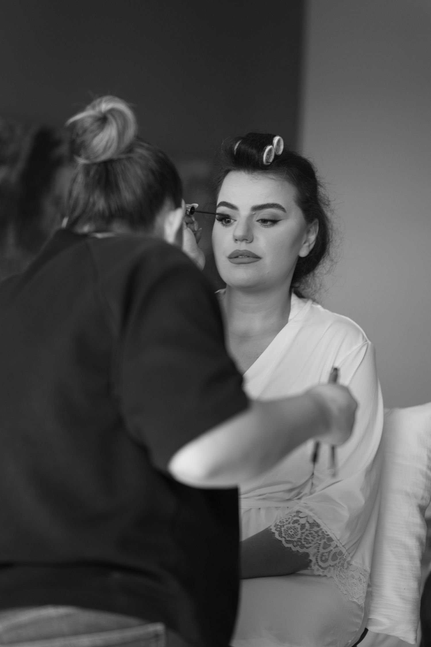 A black and white image of a makeup artist applying cosmetics to a client wearing a white robe.