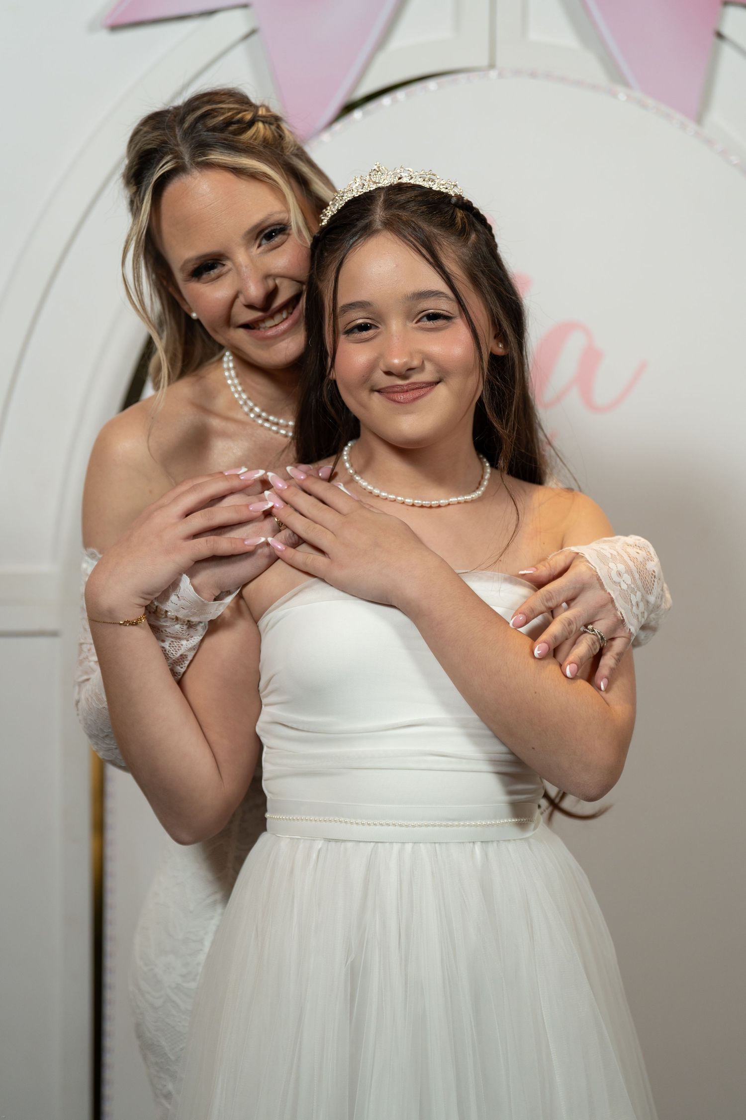 A tender moment shared between two people in white dresses against a light background during a special occasion.
