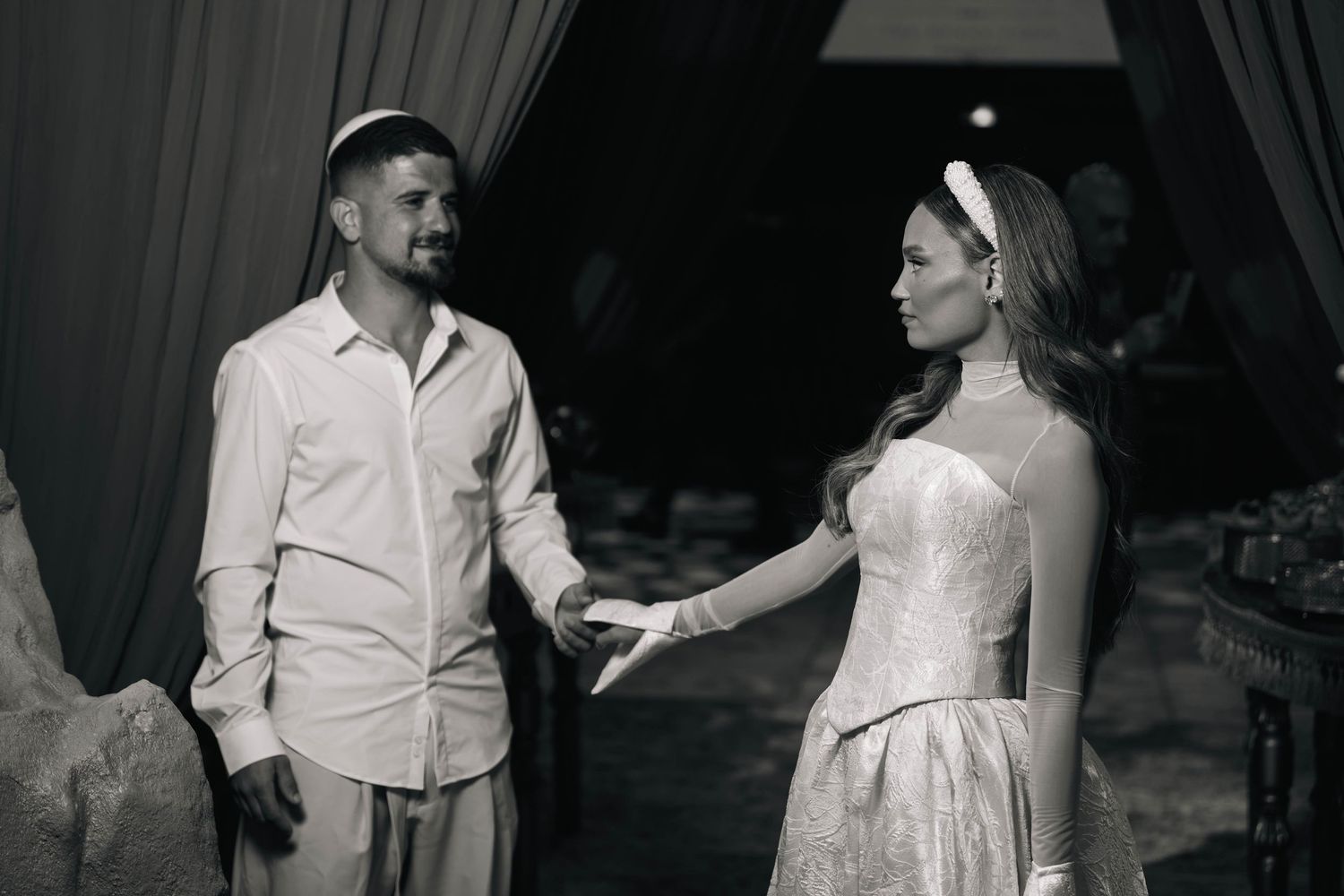 Black and white photo of a couple in formal attire, woman in strapless gown reaching toward man in casual wear.