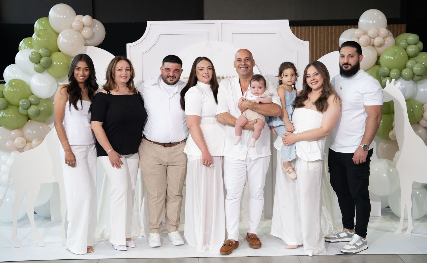 Family portrait session with coordinated white and neutral outfits against a decorated backdrop with balloons.