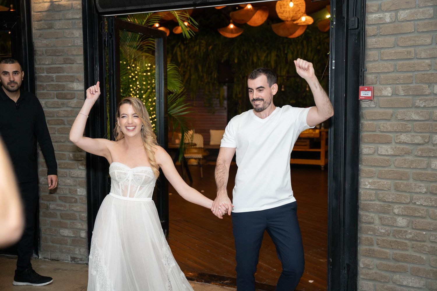 Wedding guests dancing and celebrating in a brick-walled venue with warm lighting.