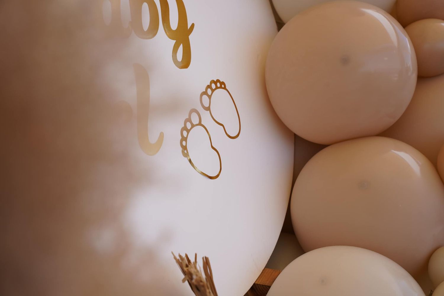 Gold baby footprint design on white wall with blush balloon decorations.
