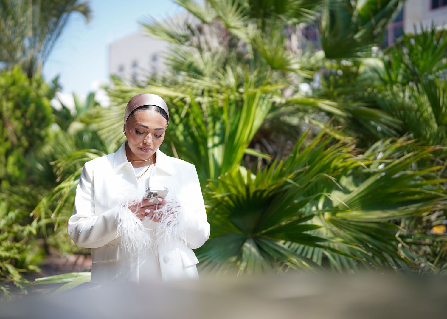 Person in white outfit stands elegantly among tropical palm trees.