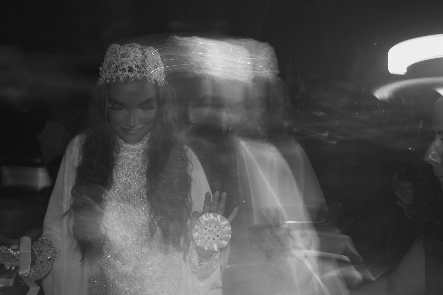 Blurry black and white photo of a bride in a lace gown and crown holding a bouquet, with ghostly double exposure effect.